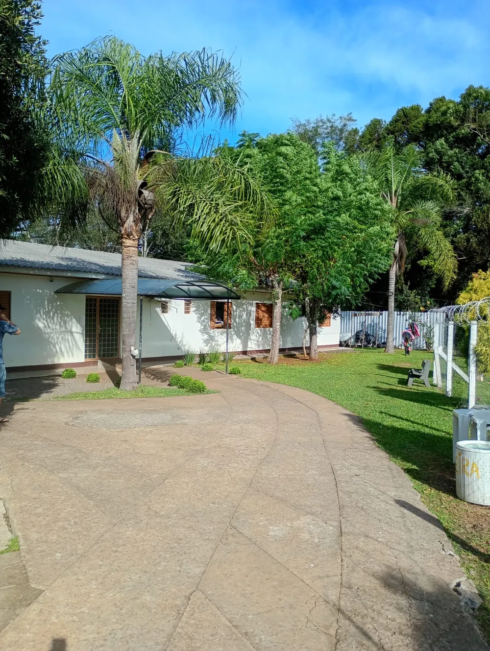 Entrada da unidade com caminho curvo, palmeiras e gramado