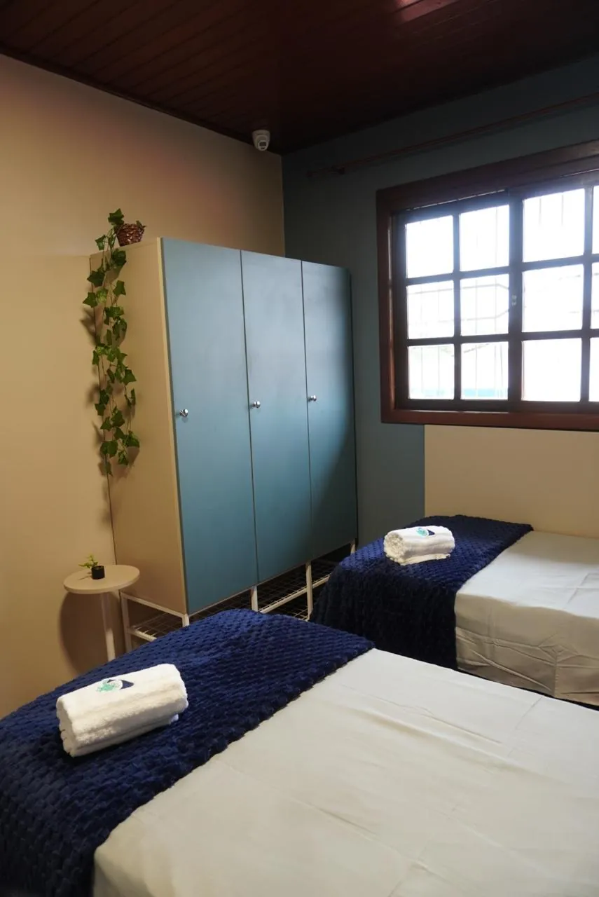 Quarto com armário azul, janela de madeira e cama com toalhas