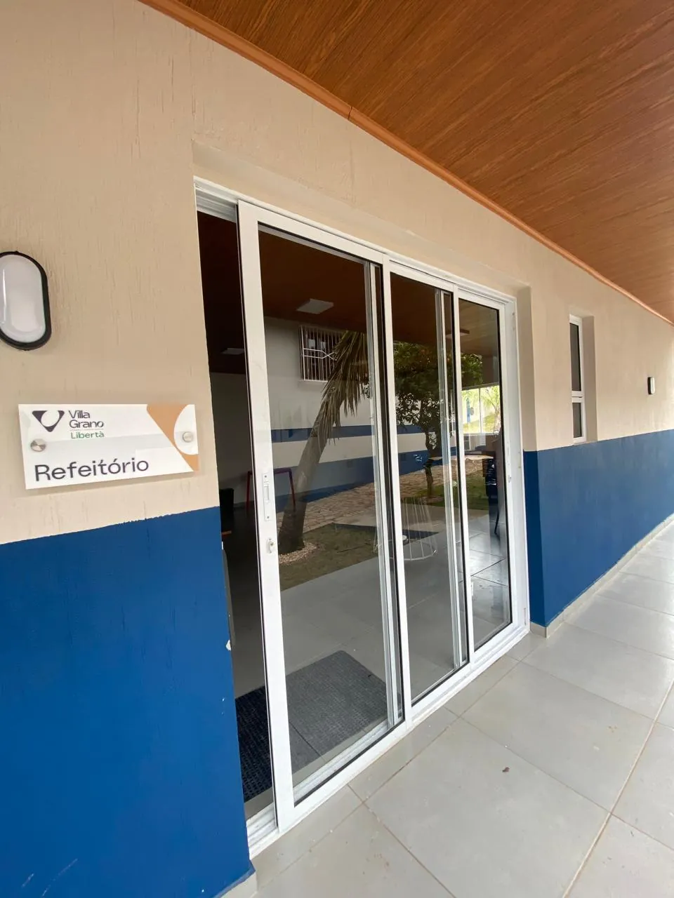 Entrada do refeitório com porta de vidro e placa de identificação