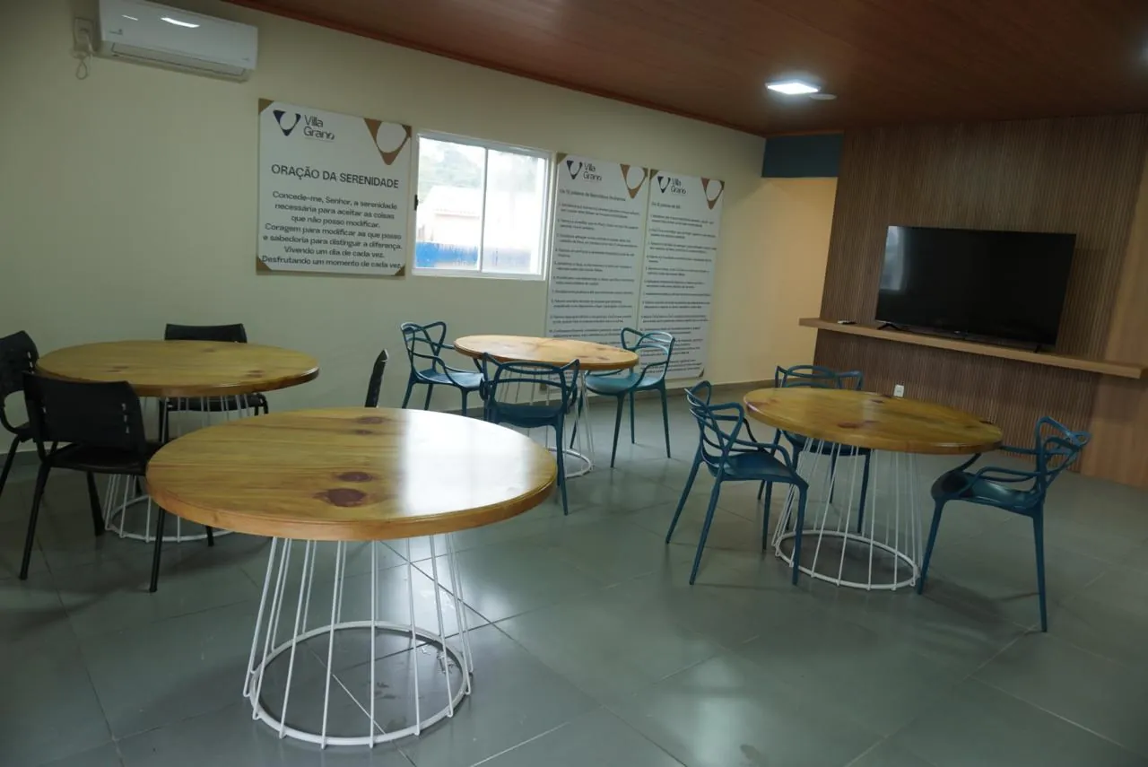 Refeitório com mesas redondas de madeira, cadeiras e televisão
